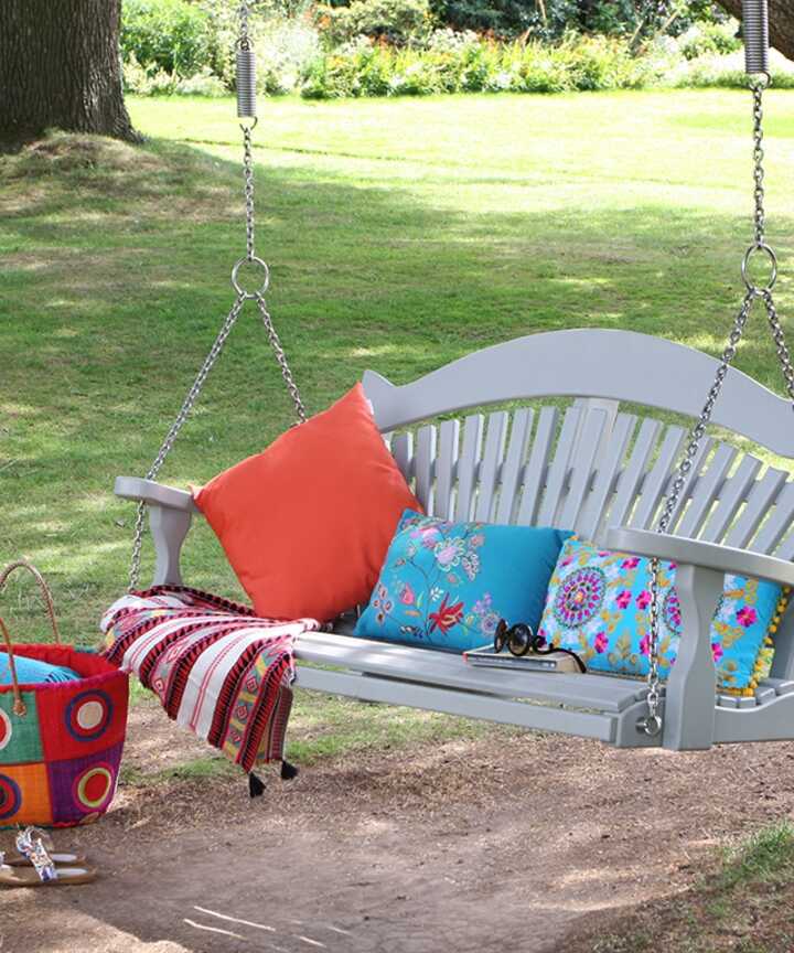 A painted swing bench hanging from a tree, with cushions and a picnic basket